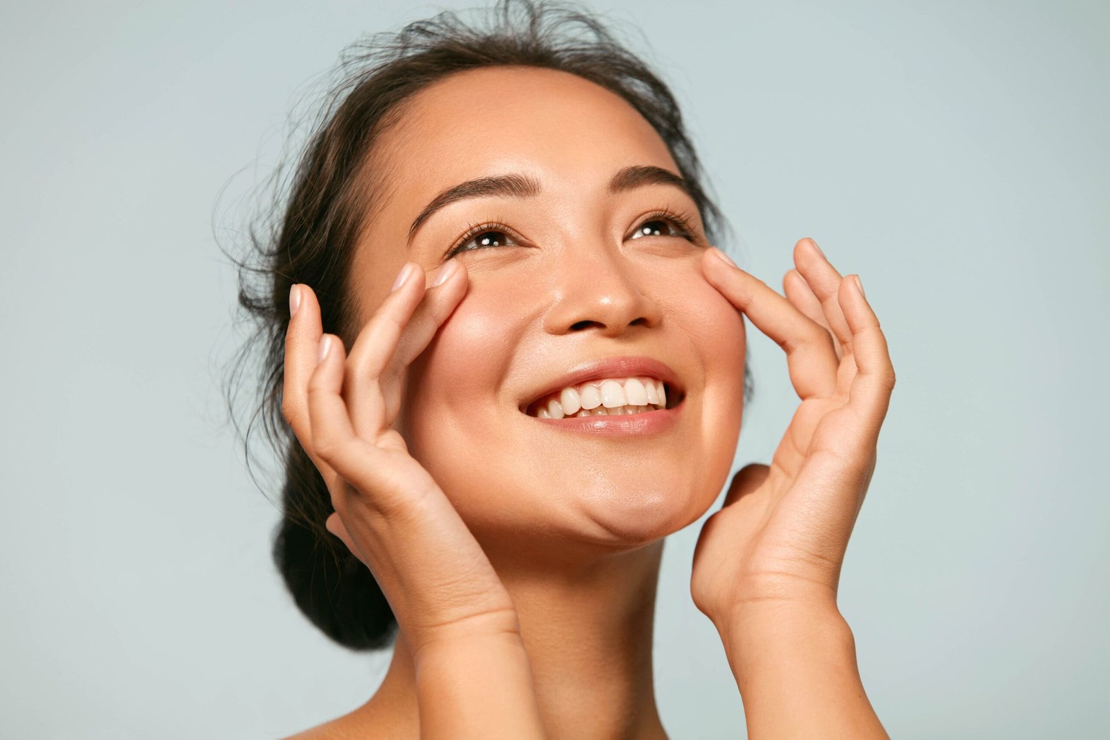 Skin care. Woman with beauty face touching healthy facial skin portrait. Beautiful smiling asian girl model with natural makeup touching glowing hydrated skin on blue background closeup; Shutterstock ID 1543602947; Purchase Order: -