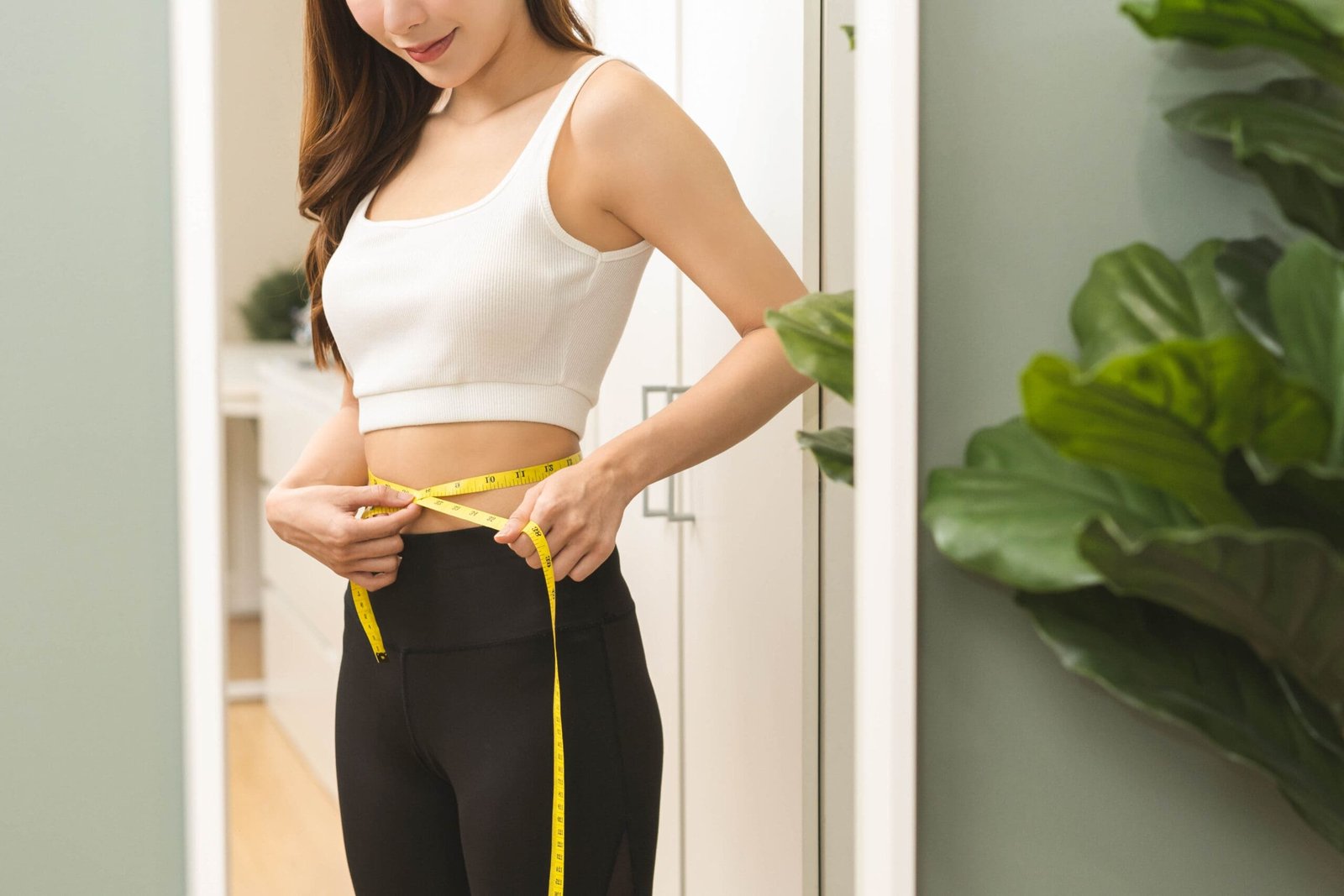 Weight lose, loss concept. Slim body asian young woman hand use tape measuring around waistline in fit sports. Girl looking reflect in mirror at home. Healthy nutrition, fitness for wellbeing beauty.; Shutterstock ID 2402389227; other: -; purchase_order: -; client: -; job: -